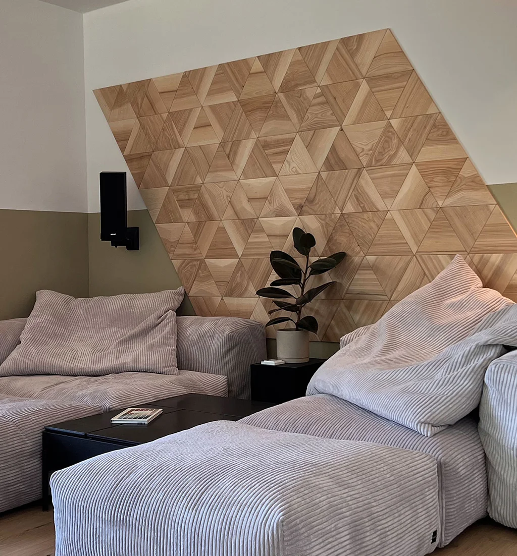 Minimalist wall decoration made of flat oak wood triangles in a living room with a light grey corduroy sofa and a houseplant.