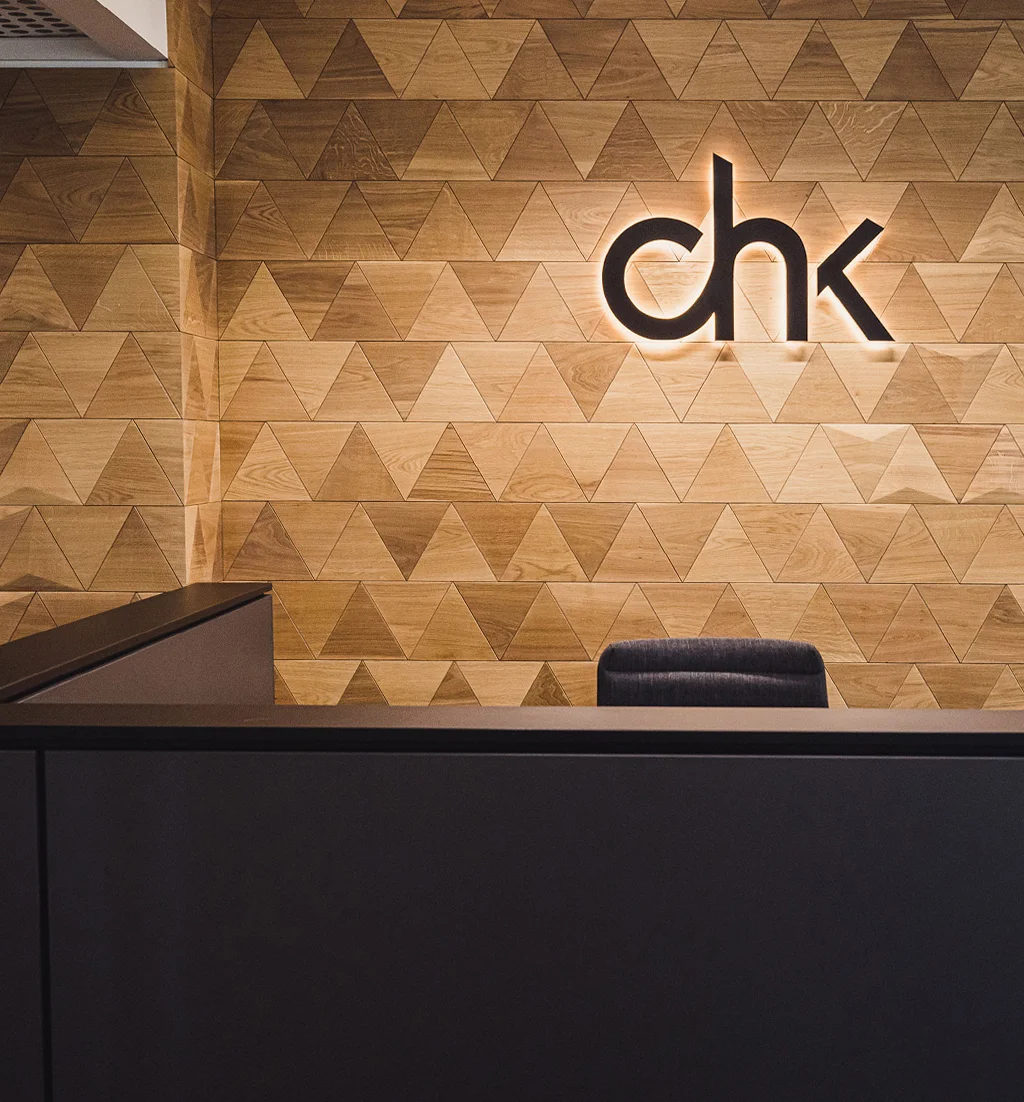 Office reception wall featuring natural oak triangle wood panels and a modern backlit company logo.