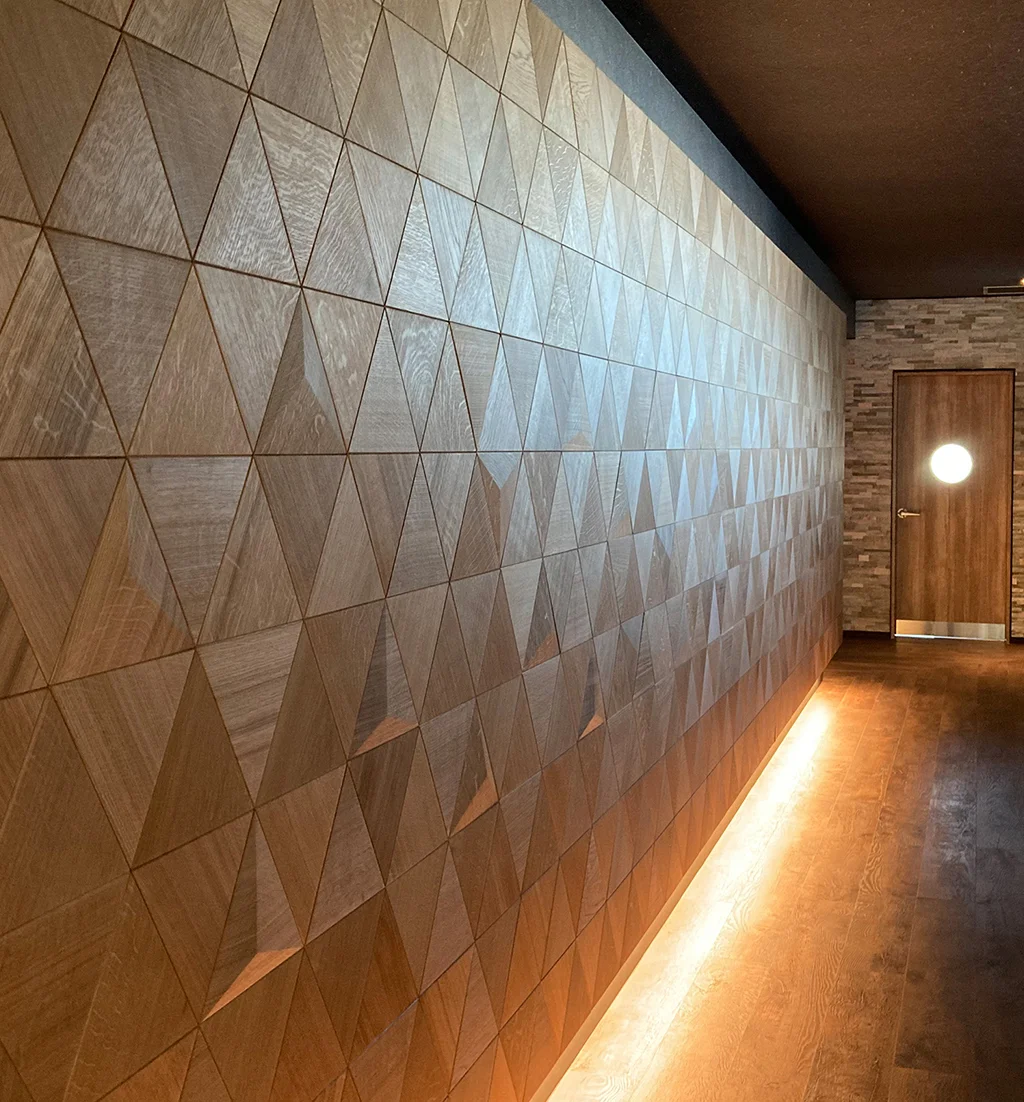 Long hallway wall featuring oak triangle wood panels enhanced by warm floor-level LED strip lighting.